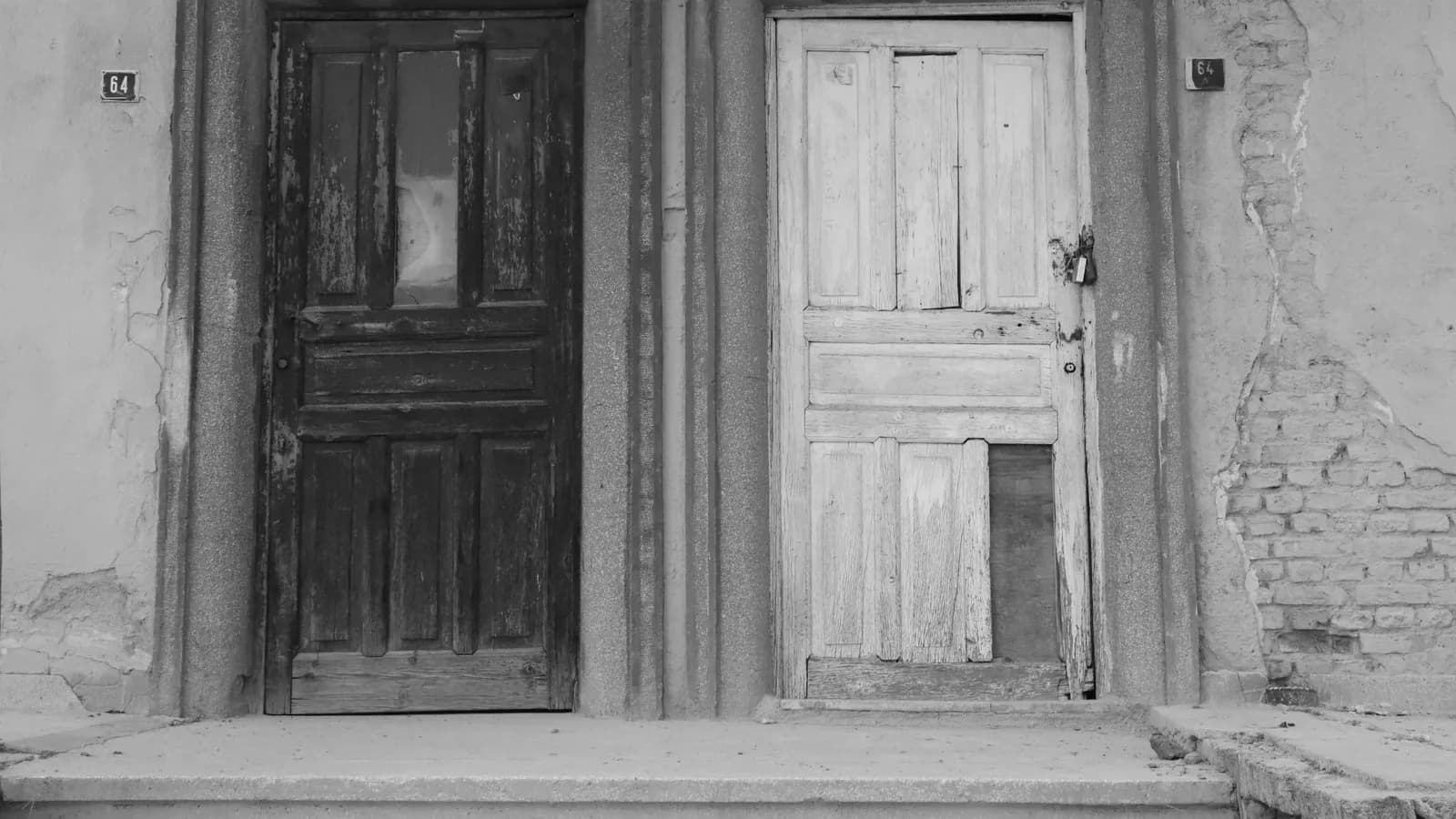 Two differently colored wooden doors side by side on an old building facade, in black and white, each marked with the number 64.