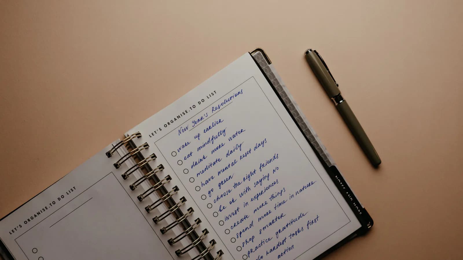 A handwritten list in a spiral notebook with a pen beside it — words jotted down but not yet checked.