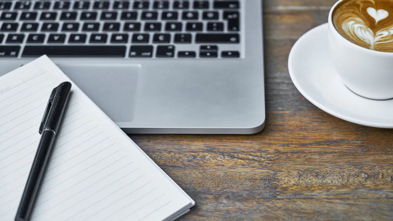 An open notebook on a desk next to a laptop and a cup of coffee, morning light coming through the window.