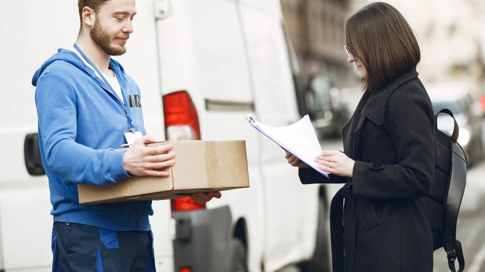 A courier stands beside a delivery van on a city street, about to carry a package to its address.