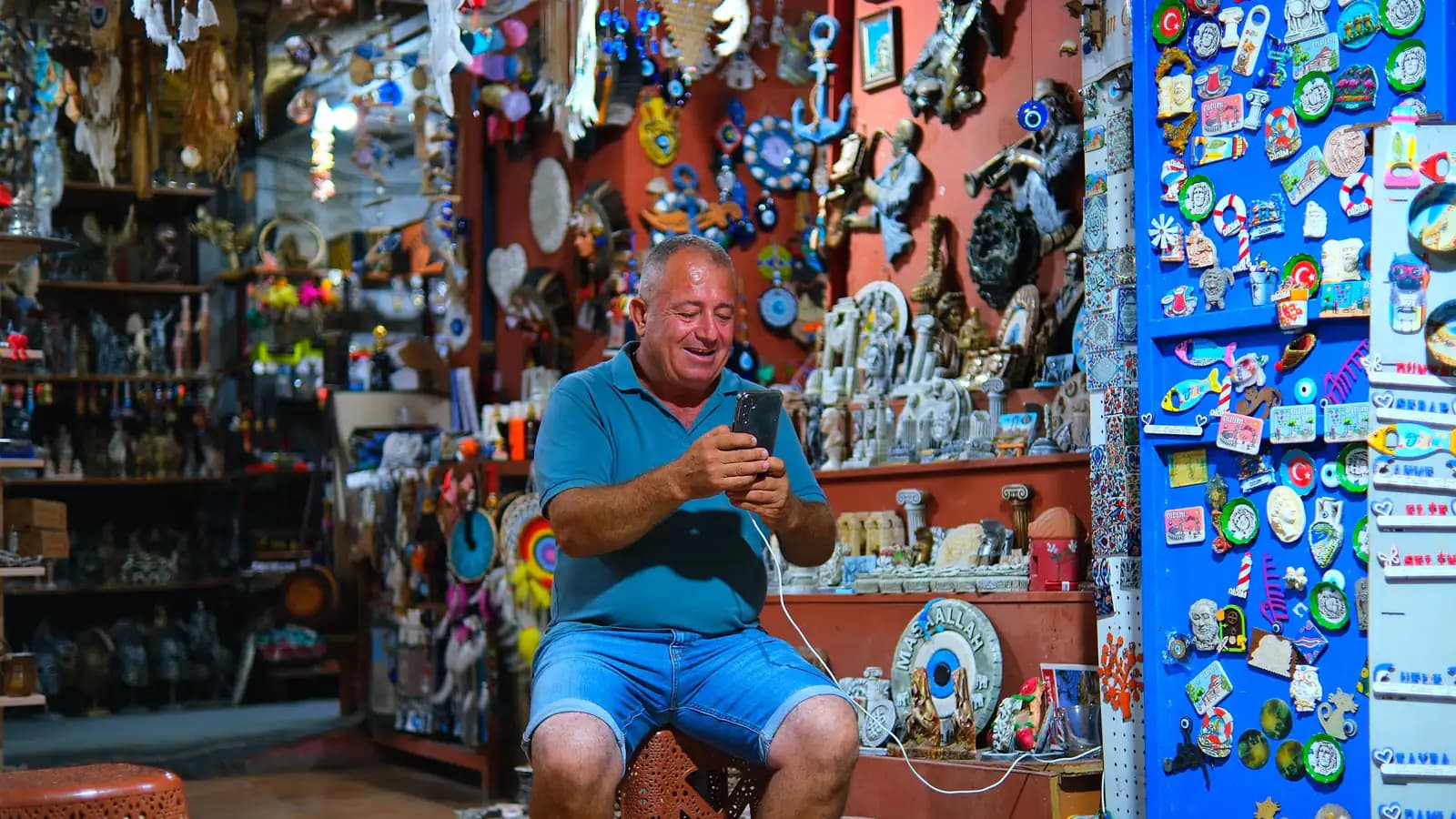 A small shop owner standing behind the counter, checking something on a smartphone.