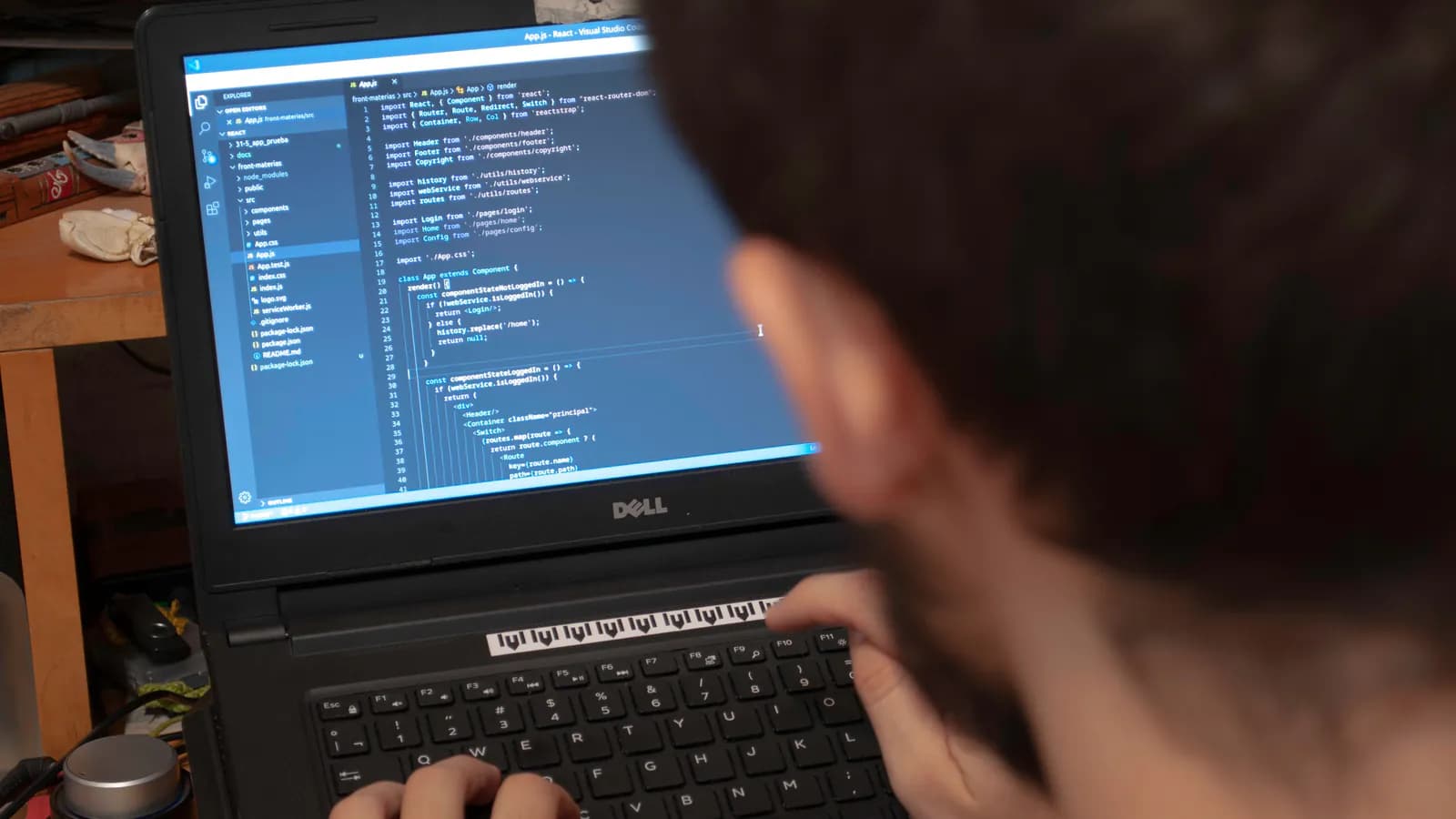 A developer's laptop screen in a dark room shows lines of mobile app code, with a smartphone resting beside it.