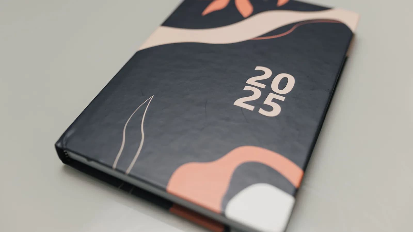 Açıq rəngli səthin üstündə üzərində 2025 yazılmış tünd cildli gündəlik — planlaşdırılmış günlərin dəftəri.