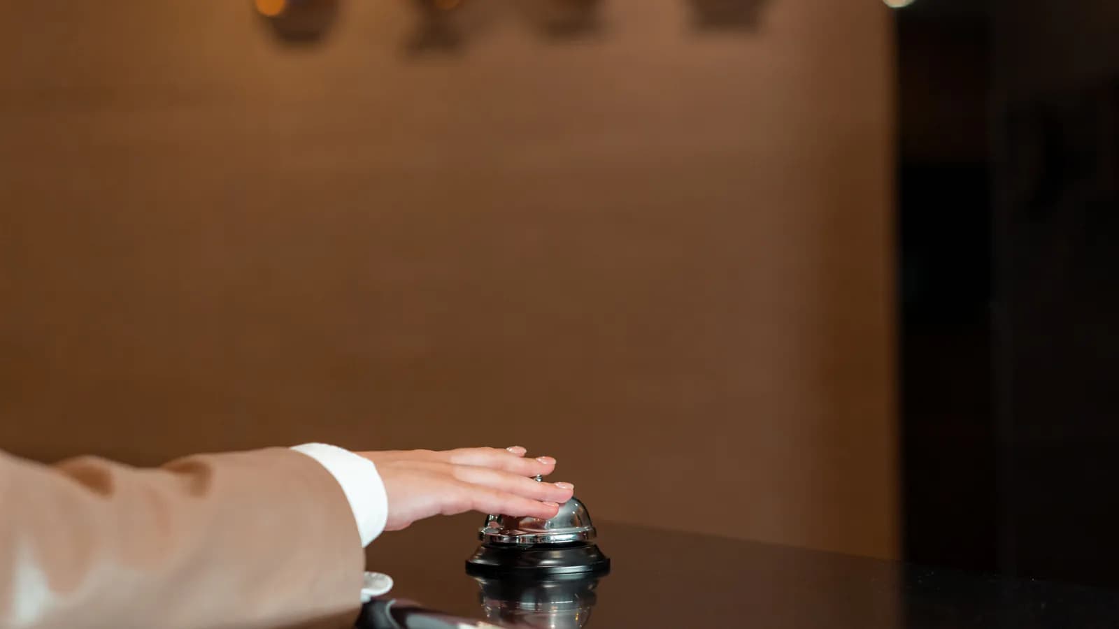 A hotel front-desk employee looks at a booking calendar on a computer screen, with room keys hanging on the wall behind the desk.