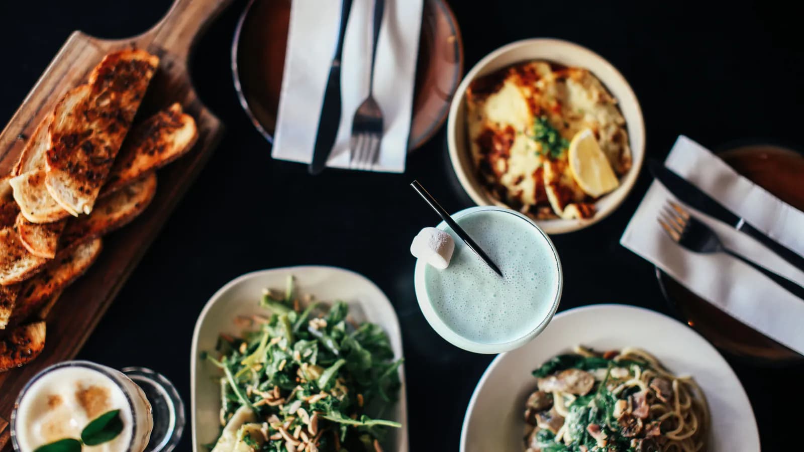 A restaurant table shot from directly overhead, several plates of food and drinks arranged across it.