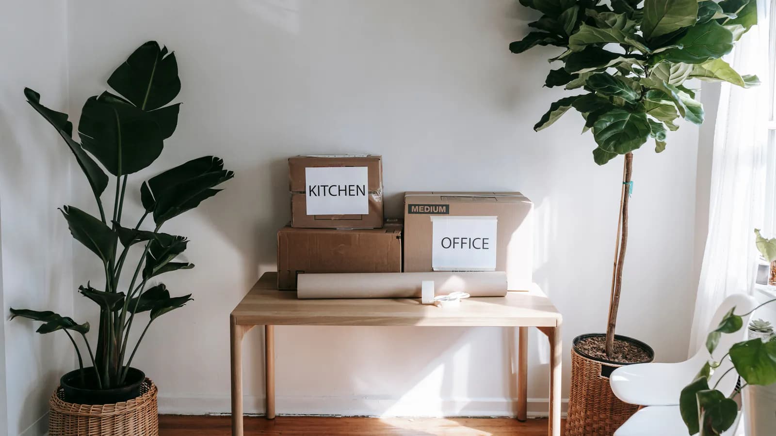 Cardboard moving boxes stacked on an office desk with empty shelves visible in the background.