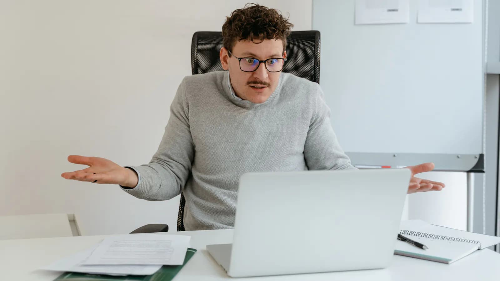 A person sits at a laptop looking confused, one hand on their forehead, while a cluttered website interface shows on the screen.
